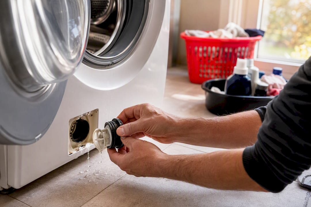 Hands removing washing machine pump filter