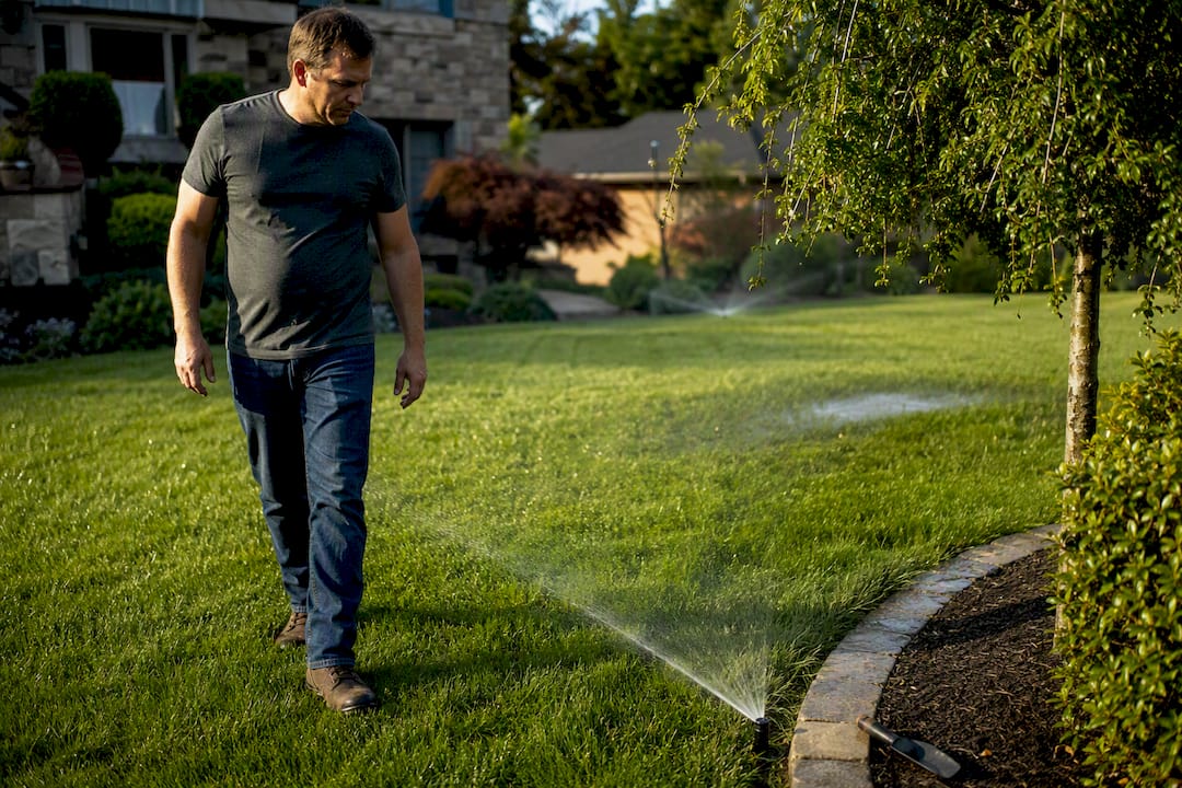 Homeowner inspecting a misaligned sprinkler head